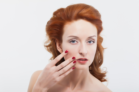 Beautiful woman touching face, clean skin, red hairs, red nails  White isolated background の写真素材