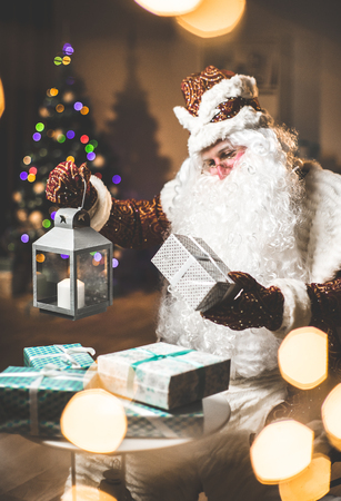 Santa brings and distributes gifts. Santa Claus with a candle lantern looking at gifts. . Cristmas tree.の写真素材