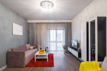 View on the window in living room. Laid table with fruits. Tv and furniture.
