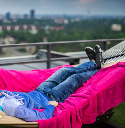 View of the city from rooftop terrace. A man resting in a hammock. Relaxation.の写真素材