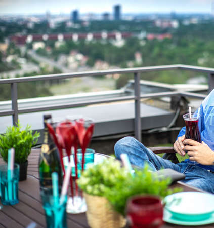 A man with cocktail in his hands seating on the rooftop terrace. Relaxing zone.の写真素材