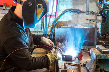 Electric welding process. Worker in welding mask. Yellow sparks fly to the sides. Bright white.