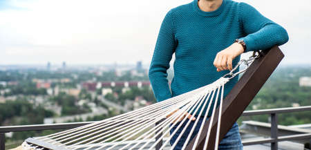 A man in a blue knitted sweater on the rooftop terrace. View of city from the top.の写真素材