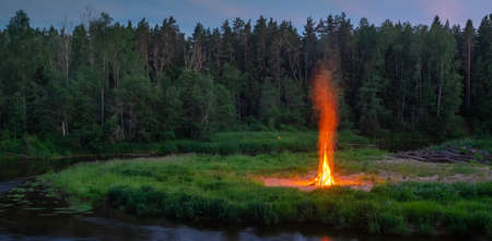 Traditional midsummer Ligo celebration. Huge bonfire on the river shore. Scenic landscape of forest at twilight.の写真素材