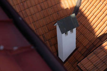 Close-up of white chimney pipe on the red tile roof in the shadow.の写真素材