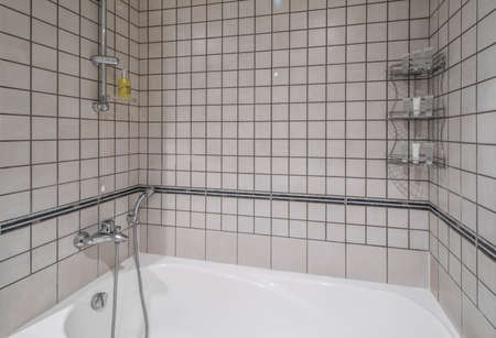 Modern interior of bathroom. Light tile. White bath with shower.