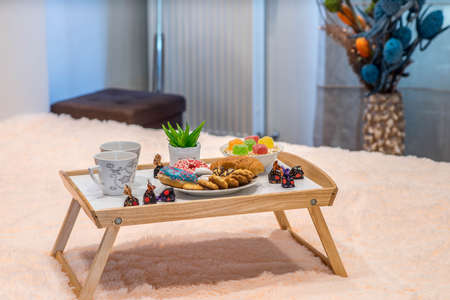 Close-up of wooden tray on the bed. Romantic breakfast. Plate with bakery. Green flower.
