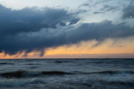 Dramatic sunset over Baltic sea. Sea waves at long exposure. Lighthouse.の写真素材