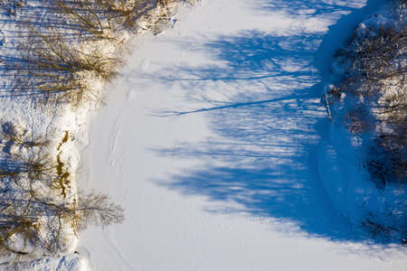 Top drone view of scenic winter forest and frozen river. Beautiful landscape. Green trees and blue shadows on white snow. Latvian nature.の写真素材