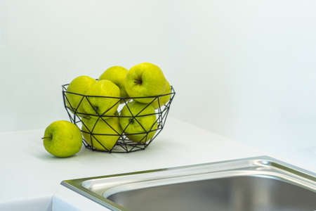 Metal sink and faucet. Green apples in vase. White counter of kitchen set. Modern interior.の写真素材