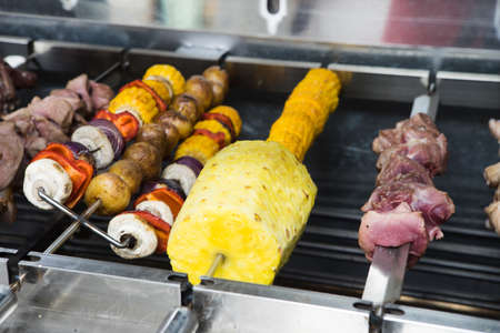 Meat, mushrooms, corn and pineapple on skewers on electric grill.の写真素材