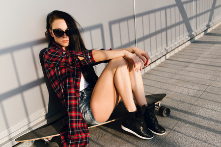 Fashion portrait of a girl in sunglasses near the wall with a skateboardの写真素材