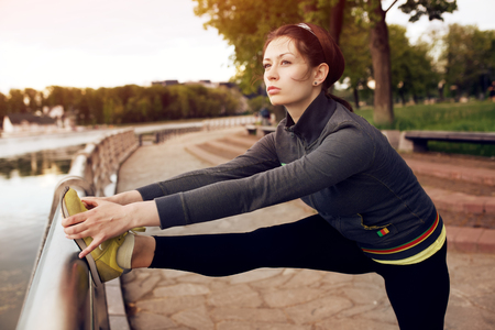 Yong female runner with beautiful figure doing stretching exercise before began her run in the city park near the lakeの写真素材
