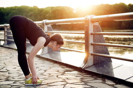 Beautiful young girl doing stretching in the summer at sunset in the city park near the lakeの写真素材