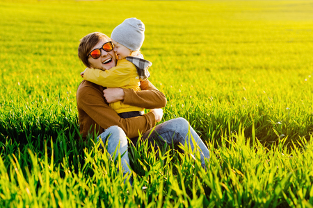Young father resting with his young son on summer field at sunsetの写真素材