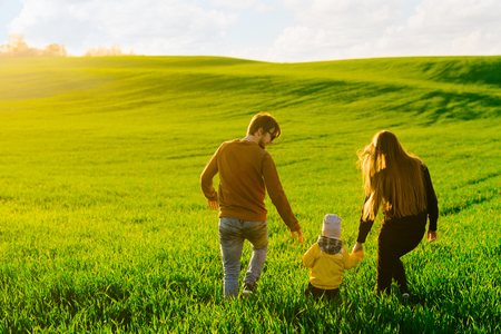 Young parents with a young son walking on a field at sunset in the summer. Concept of familyの写真素材