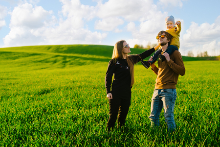 Young parents with a young son walking on a field at sunset in the summer. Concept of familyの写真素材