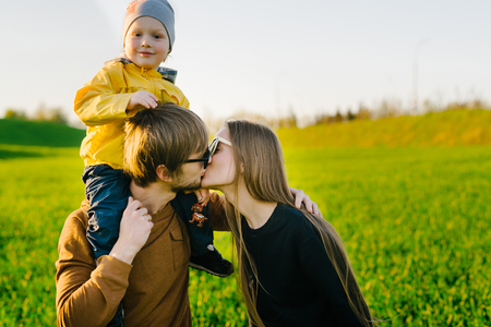 Young parents with a young son walking on a field at sunset in the summer. Parents kiss each other. Concept of familyの写真素材