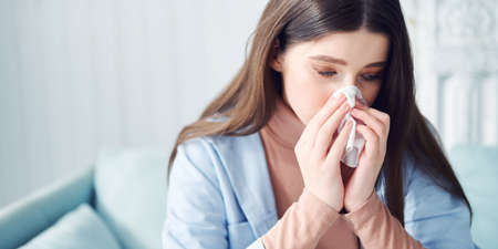 Sick girl marks in handkerchief at home, running nose, flu, bowingの写真素材