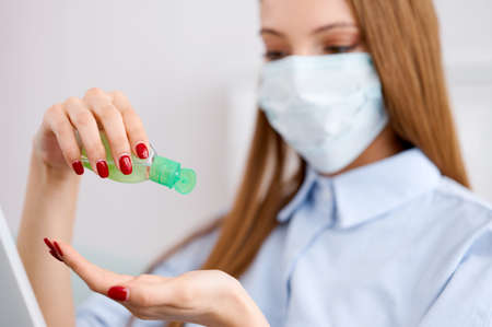 Teenage girl uses antibacterial gel for hands, working in protective medical mask in quarantine....
