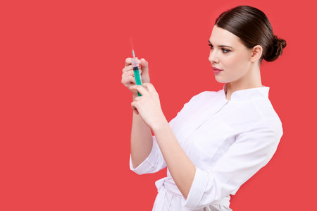 Woman doctor holding and checking syringe on red isolated background, young nurse, medical staffの写真素材