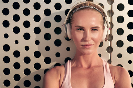Sporty woman listening to music on headphones, young slim girl in sportswear near wall in the cityの写真素材