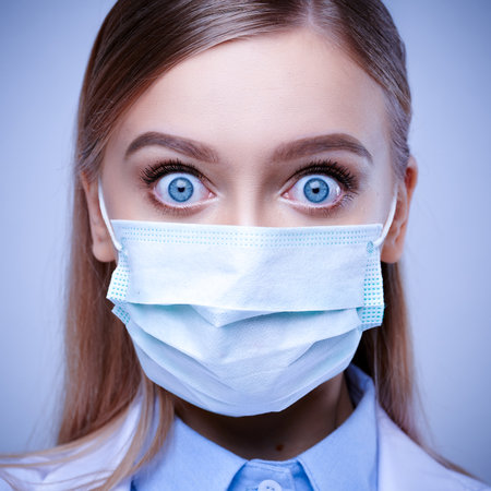 Close-up face of masked female doctor with surprise and wide open eyes.の写真素材