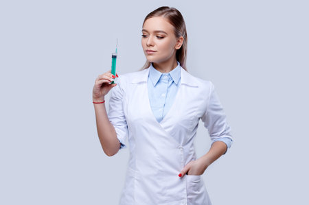 Woman doctor wearing uniform holding syringe on isolated background, young nurse, hospital staff
