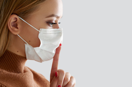 Close portrait woman in medical protective mask holds finger near lipsの写真素材