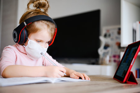 Distance learning online education. Sickness schoolgirl in medical mask and headphones studying at...