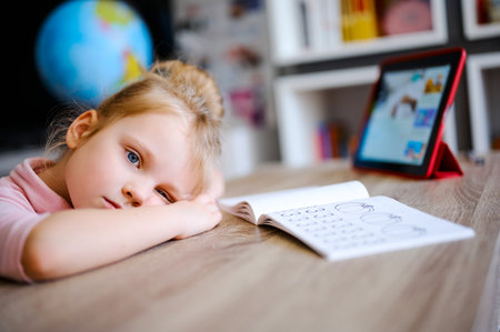 Tired young girl doing homework at home at the table. Distance Education Online Learningの写真素材