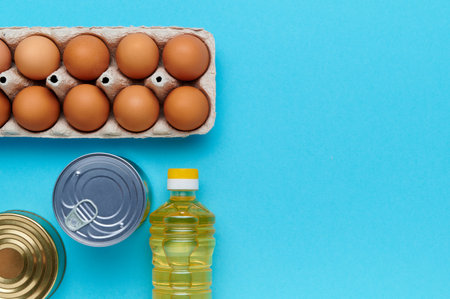 Top view, flatlay, computation, copyspace. Set of products on the blue background. Packaging food from the store. Sunflower oil, eggs, canned food, loaf of bread. Delivery and donation conceptの写真素材