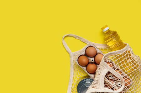 Set of products in string bag on yellow background. Food from the store in the package. Sunflower oil, eggs, canned food. Delivery and donation conceptの写真素材
