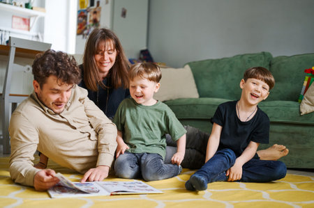 Happy family with two little sons reading story indoors, parents with children spending time together and lying on the floor at homeの写真素材