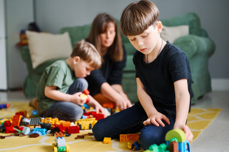 Toddler boy playing with construction blocks at home, mother and brother on the backgroundの写真素材