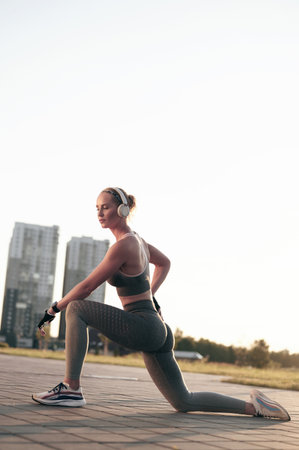 Strong sporty woman in headphones stretching outdoors