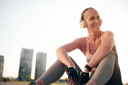 Smiling woman athlete relaxing after workout and physical exercise, listening music in headphonesの写真素材
