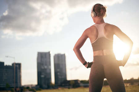 Strong fitness woman in sportswear listening music in headphones and doing physical exercise outdoorの写真素材