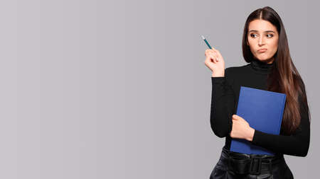 Thoughtful concentrated busy woman holds pencil and notepad, female student with an exercise book...