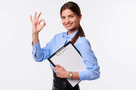 Businesswoman holding folder on white isolate background. Smiling caucasian female worker in uniform showing thumb up gestureの写真素材