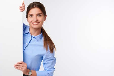 Attractive businesswoman in shirt holding white blank billboard and smiling on white isolated backgroundの写真素材