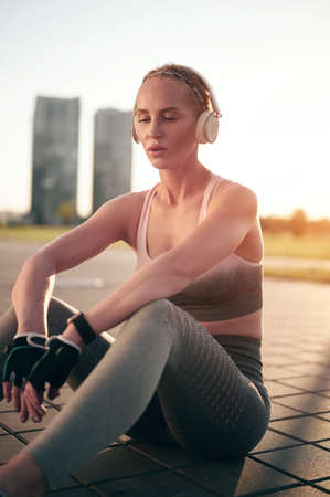 Exhausted strong woman in headphones and fitness wear is resting and listening music in headphonesの写真素材