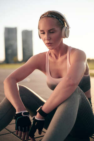 Exhausted woman in fitness wear relaxing after physical exercise and listening music in headphonesの写真素材