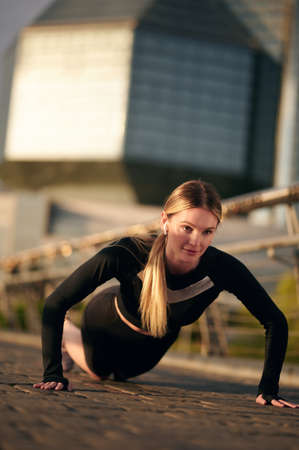 Athlete woman in sportswear doing push ups on the bridge before running in urban training workout....