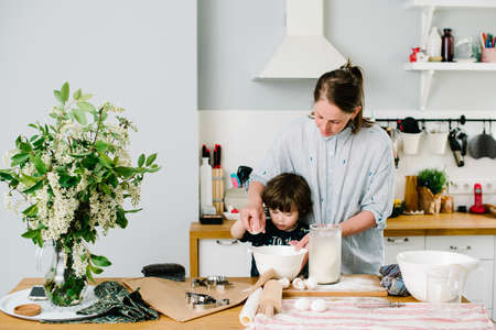 Little boy helping his mother with the baking in the kitchen standing at the counter alongside her kneading the dough for the pieの写真素材