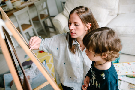 Young mother drawing chalk on blackboard with his young son at homeの写真素材