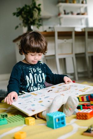 Young preschool boy reading book on the floor at home. High quality photo