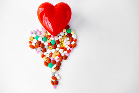 Multicolored pills on a table in the shape of a heart on a white background. Red heart. Doctor's hands on the table near the heart and pills. Top view with copy space. Medicine conceptの写真素材
