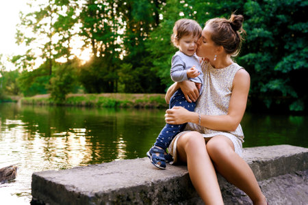 Young pregnant mother walking with her little son in summer park near the lake and feed the ducksの写真素材