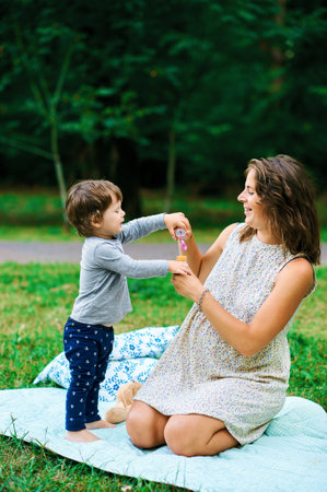 Little boy with his pregnant and happy mother blowing bubbles in the park in the summer on a lawnの写真素材